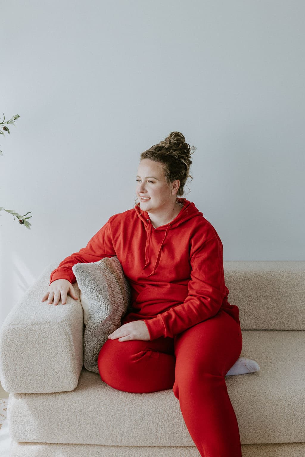Megan Nakazawa sitting on a couch in a red hoodie, smiling
